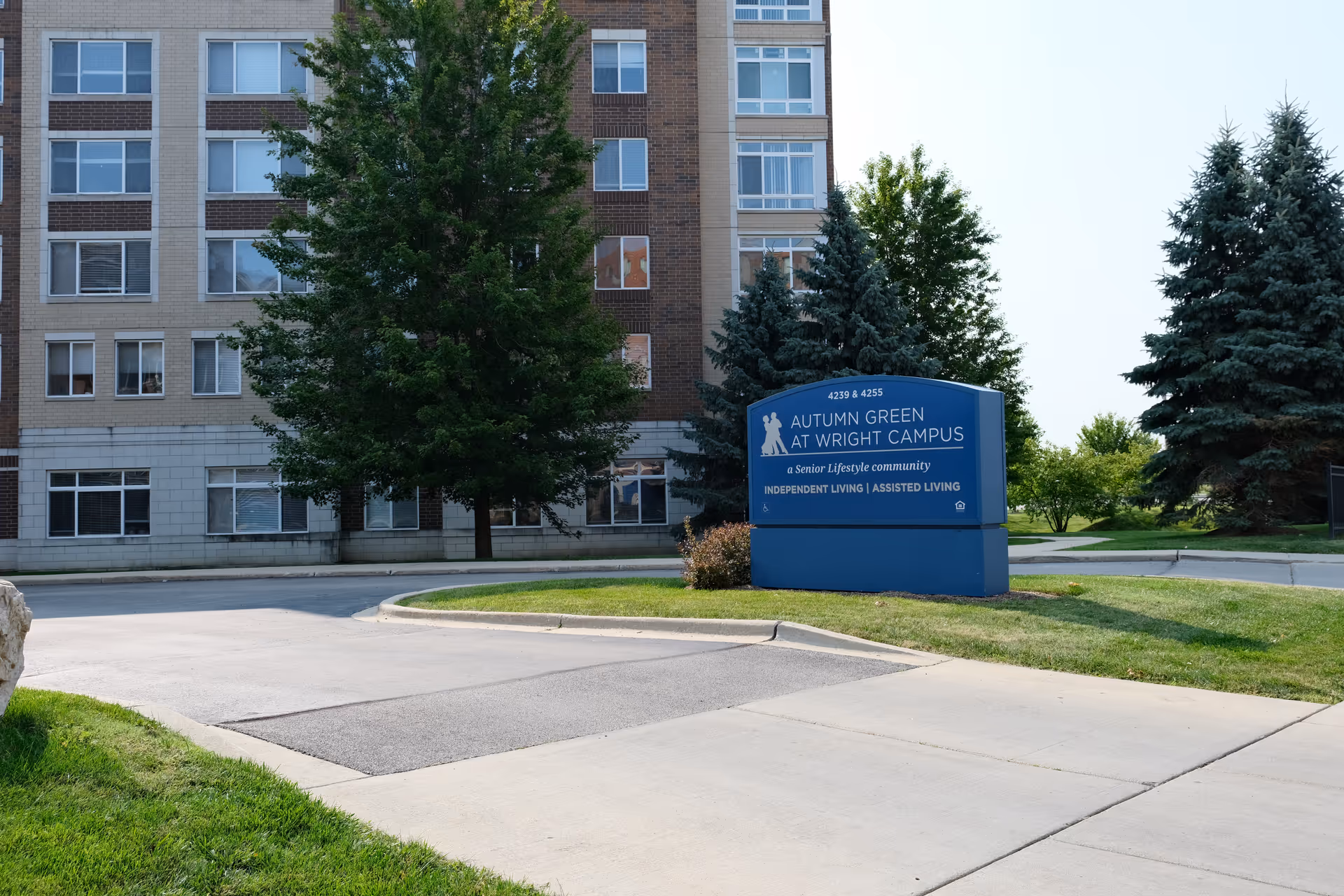 Exterior view of a multi-story senior living building with a blue 'Autumn Green at Wright Campus' sign on the lawn.