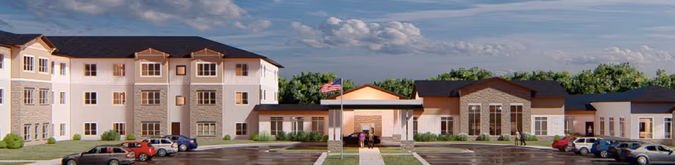 Front exterior view of Harmony Gardens Senior Living facility showing a large, multi-section building with multiple windows, a covered entrance with an American flag in front, and a parking lot with several cars parked.