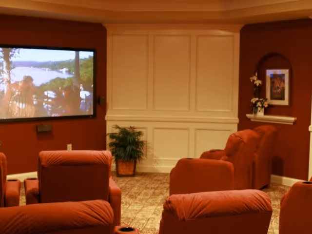 Cozy media room with red upholstered recliners facing a large wall-mounted projection screen and paneled white wall.