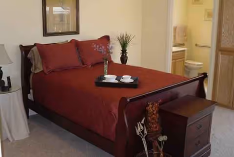 A wooden bed with red bedding and a tray with cups in a tidy bedroom.