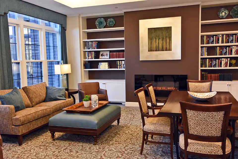 Comfortable common room with a sofa, armchairs, ottoman, dining table, built-in bookshelves, and a fireplace.