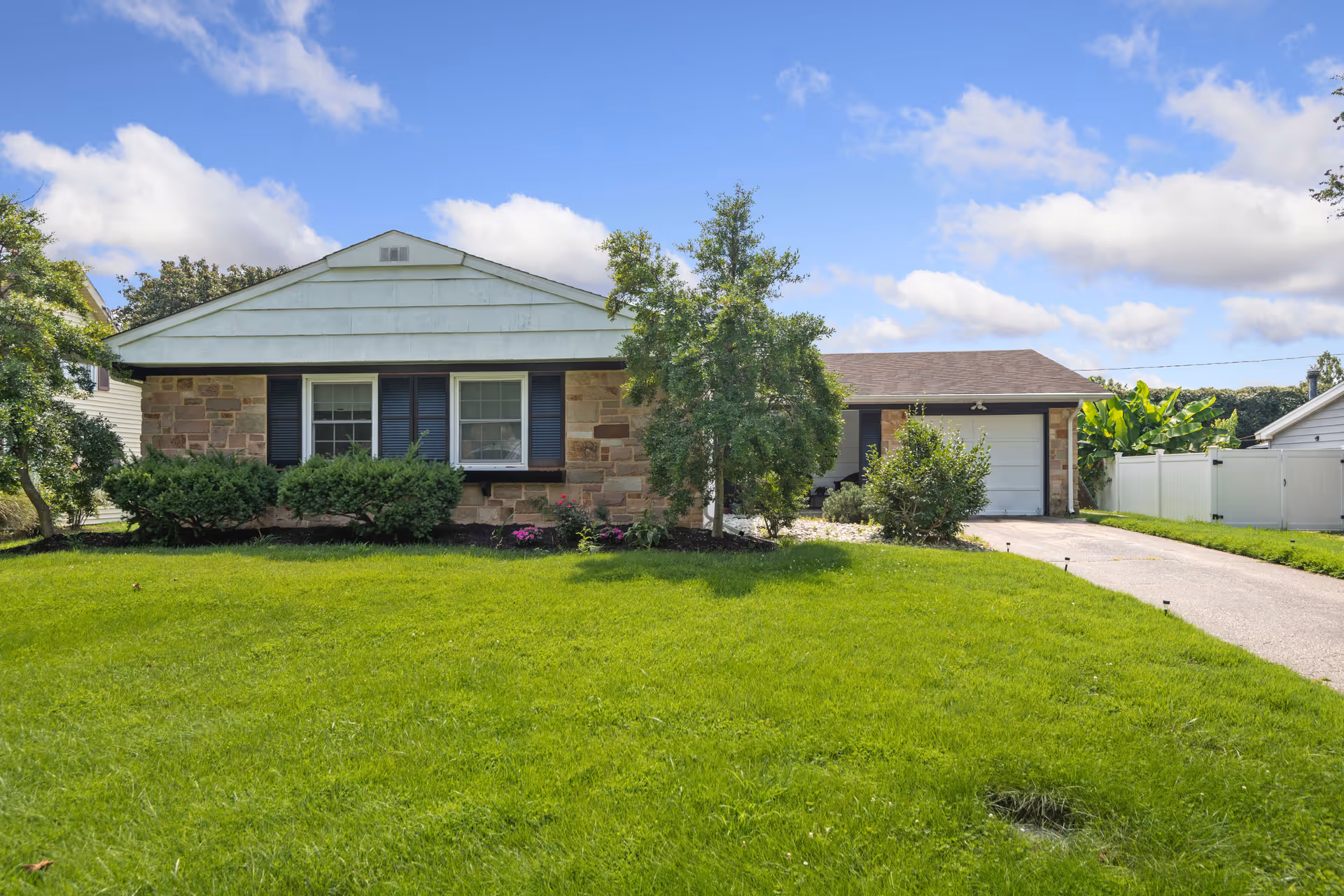 One story residential building with a green lawn, trees, and a driveway to a garage.