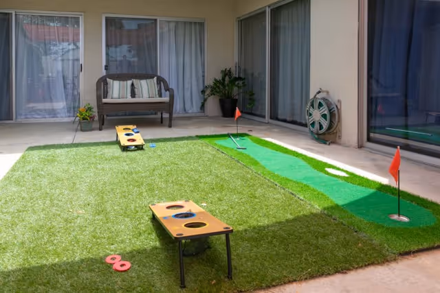 Covered courtyard patio with artificial turf featuring cornhole boards, a putting green, a bench, and sliding glass doors.