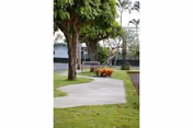 Paved walkway winding through grassy grounds with trees, a bench, and a low building in the background.