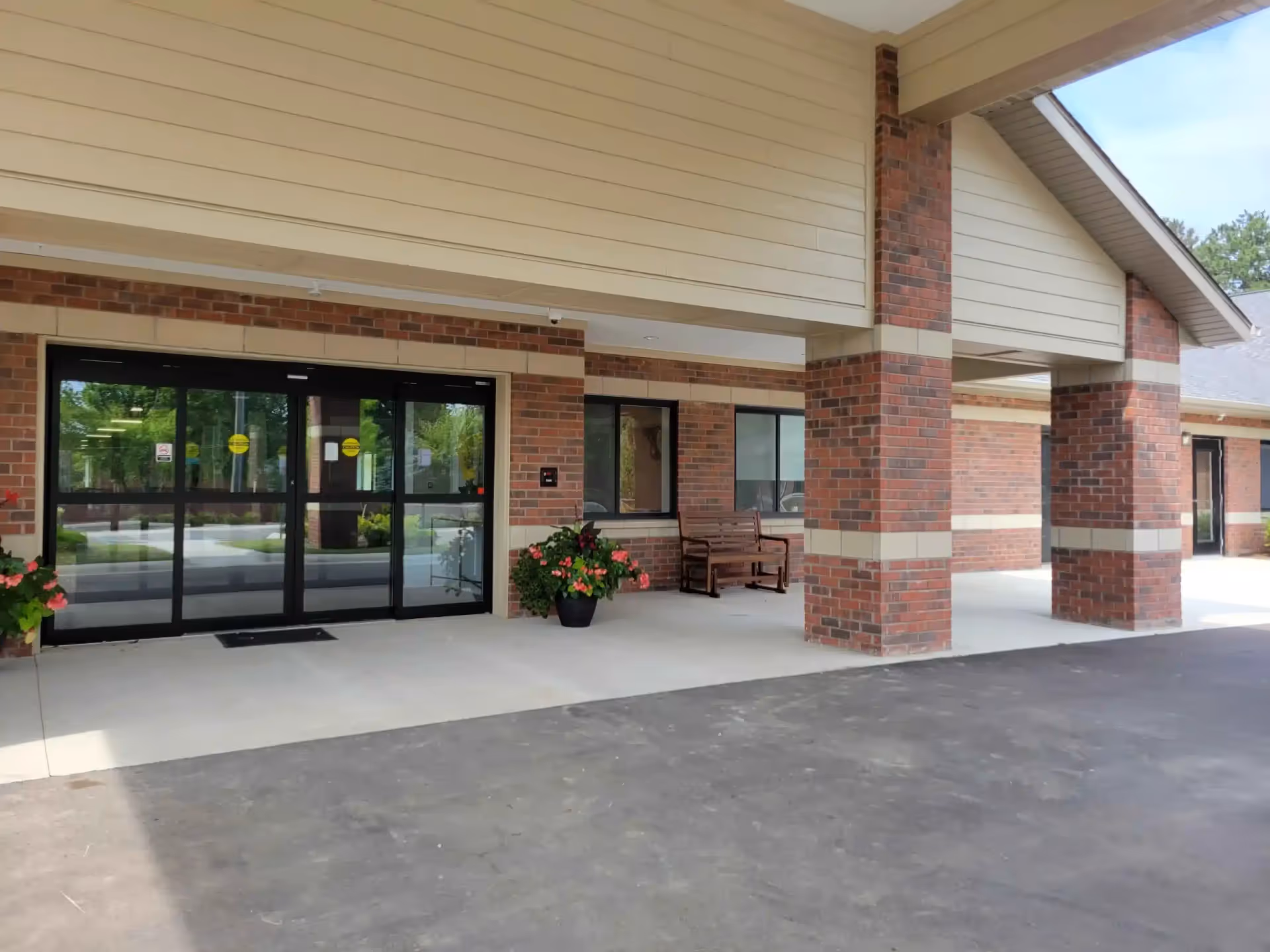 Brick exterior entrance with glass doors, brick columns, and potted plants under a covered walkway.