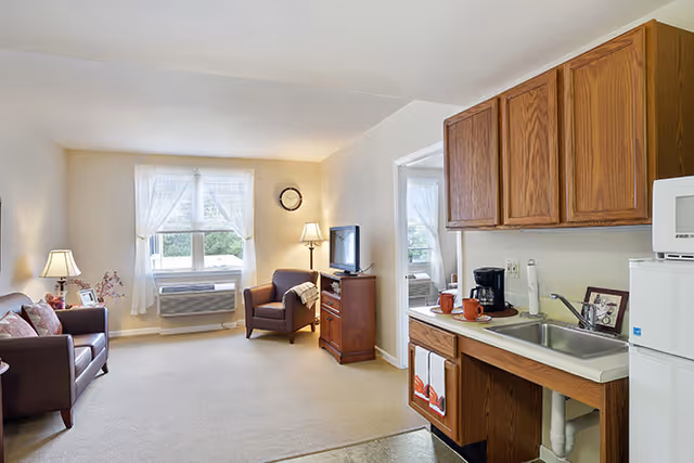 Bright open living area with seating, a TV, and a small kitchenette with sink and cabinets.