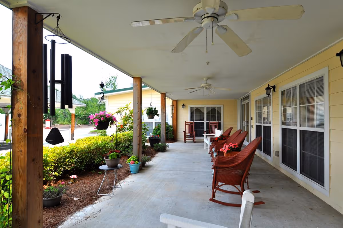 Covered front porch with red wicker rocking chairs, hanging plants, ceiling fans and potted flowers at a retirement community.