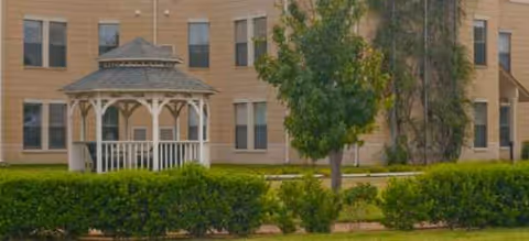 Town Village Crossing exterior with beige brick building, gazebo, trees, and hedges in front.