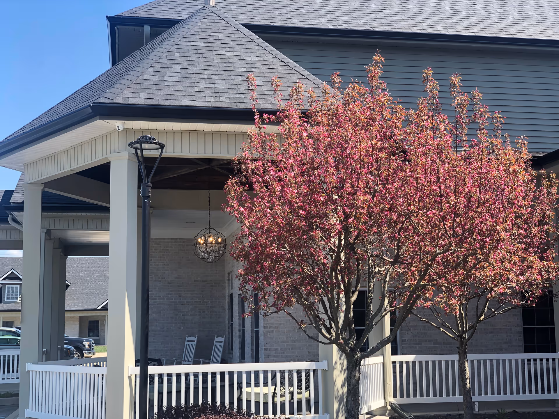 Front entrance of a building with a covered porch, white railing, and a pink flowering tree in bloom.