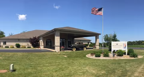 A brick assisted living facility with a porte-cochere entrance, flagpole, and manicured lawn.