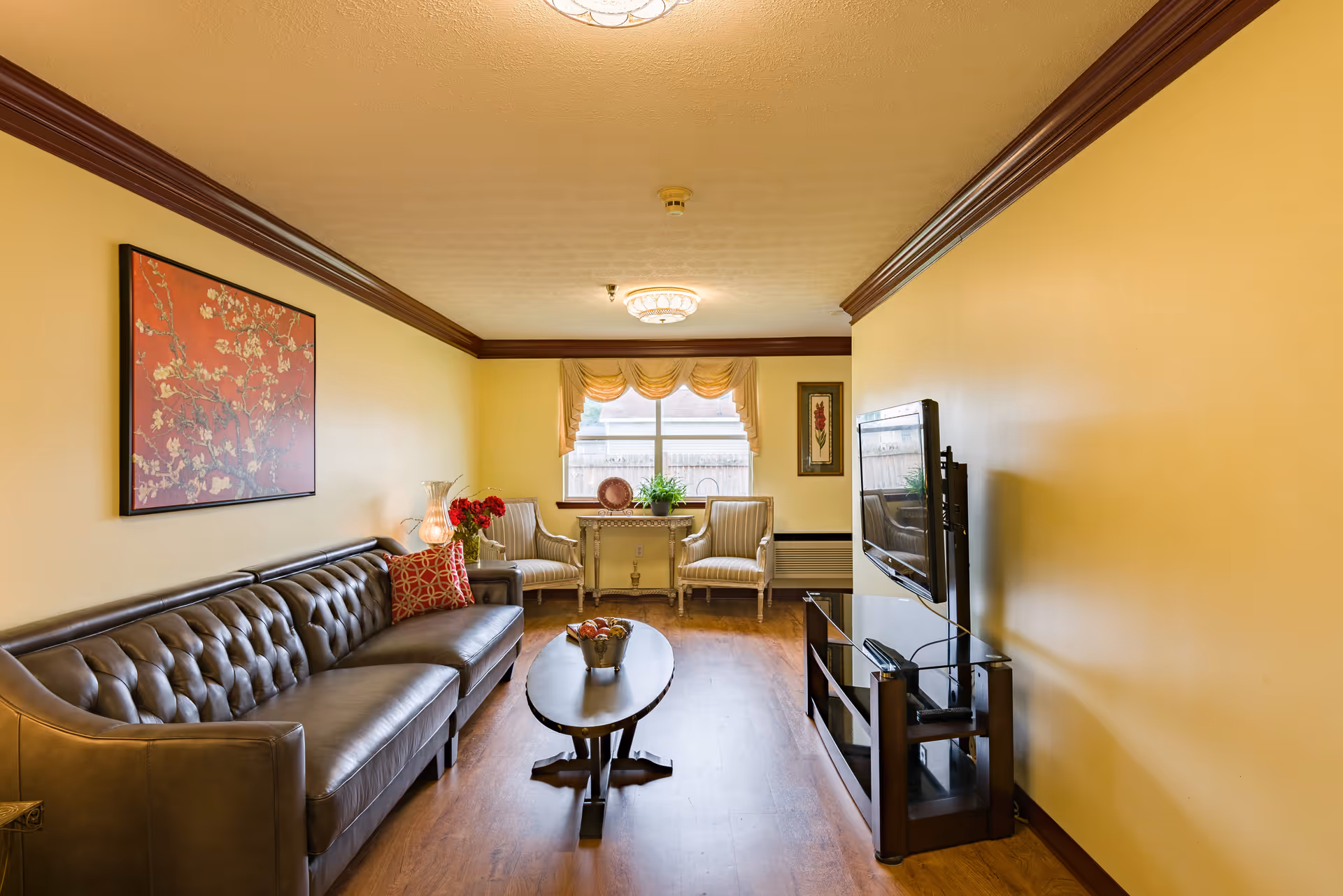 Cozy living room with a tufted leather sofa, coffee table, wall-mounted TV, and two chairs by a window.