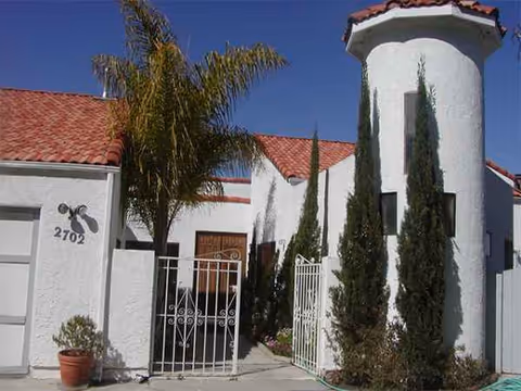 Exterior view of a white stucco building with red tile roof, gate, and tall trees.
