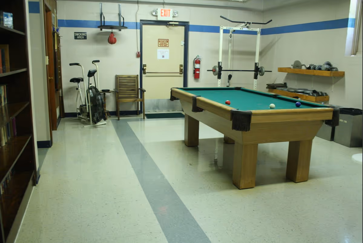 Indoor recreation room with a pool table, exercise equipment, free weights and bookshelves.