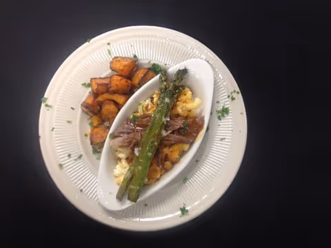 Top-down view of a plated meal with roasted potatoes, macaroni topped with shredded meat and asparagus on a white plate.