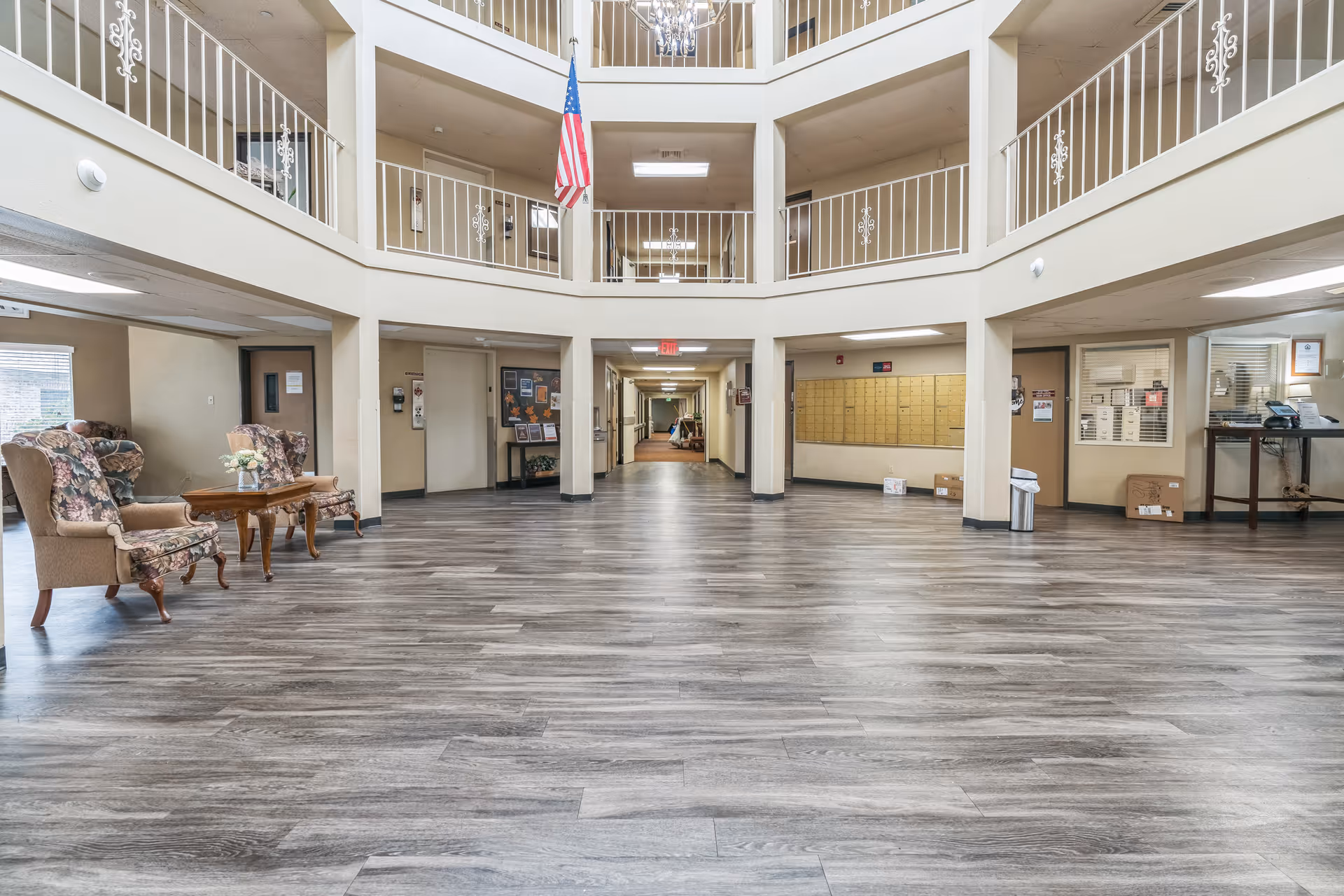 Spacious two-story atrium lobby of a senior living facility with seating, railings, an American flag and a long central hallway.