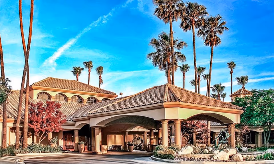Mediterranean-style building entrance with a tiled porte-cochere, palm trees, and landscaped driveway.