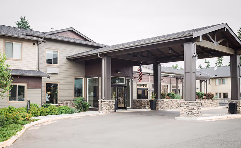 Senior living facility exterior with covered entrance, stone pillars, and landscaped driveway.