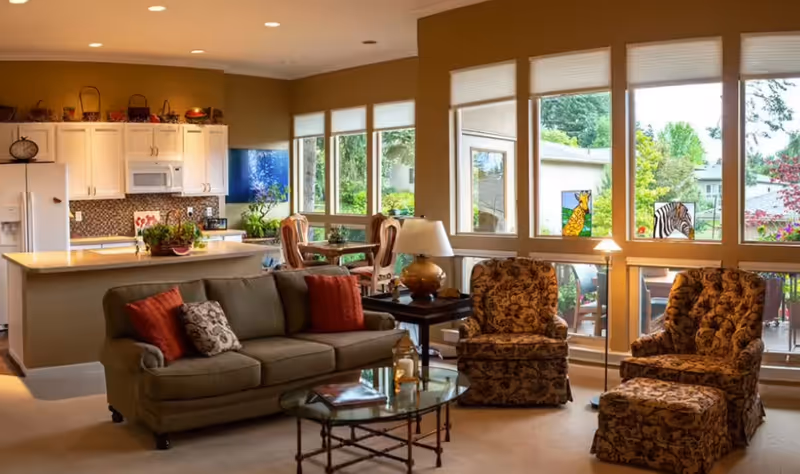 Open-concept living area featuring a sofa, patterned chairs, glass coffee table, and bright kitchen.