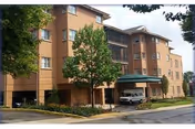 Exterior view of a multi-story brick senior living facility named Gilpin Hall with a covered entrance, several windows, a tree, and a parked vehicle near the entrance.