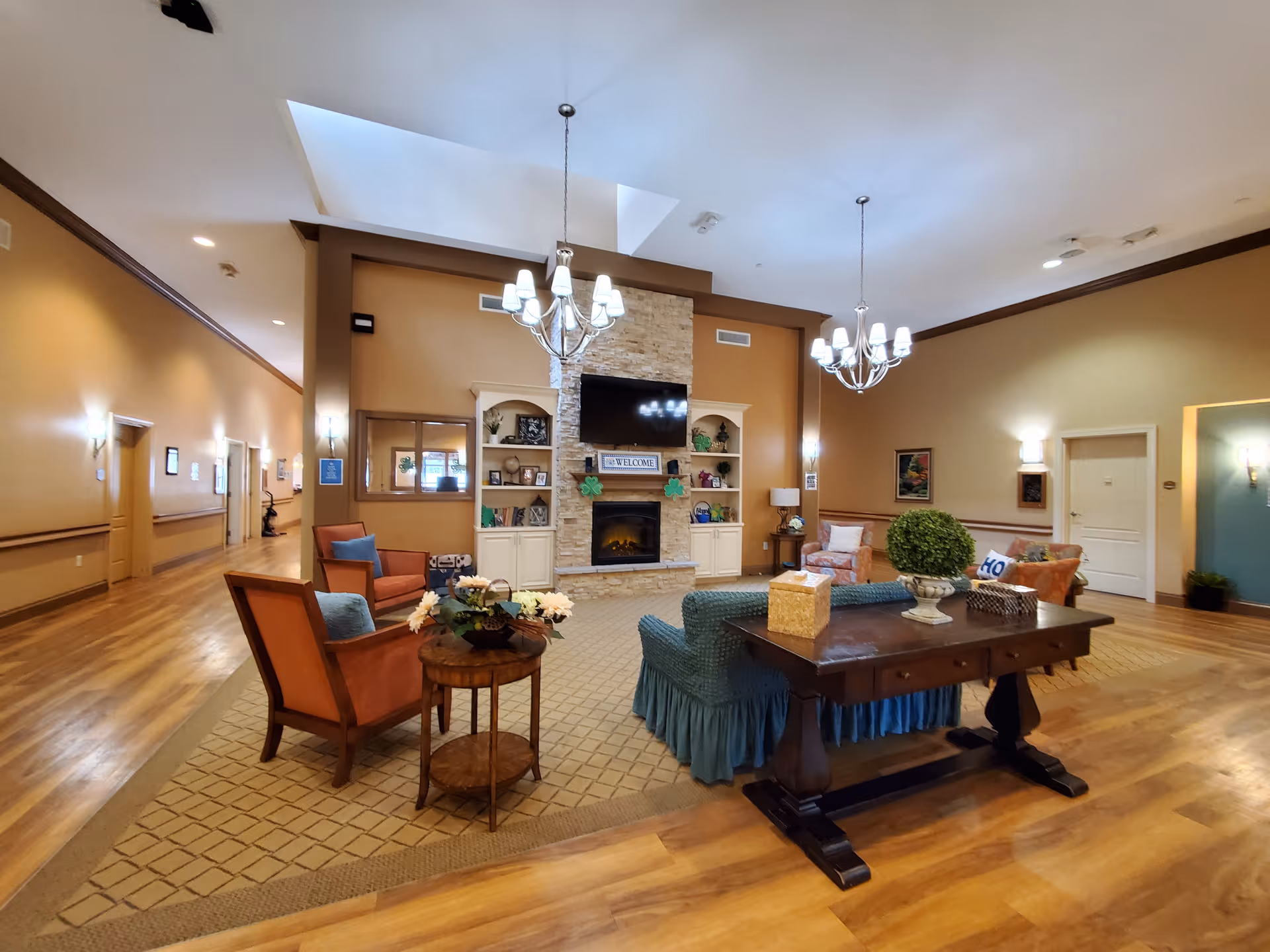 Spacious, warmly lit common living area with multiple seating areas, a central fireplace and TV, and decorative furnishings.