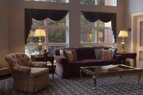A furnished living room with sofa, armchair, coffee table, lamps, and large windows.
