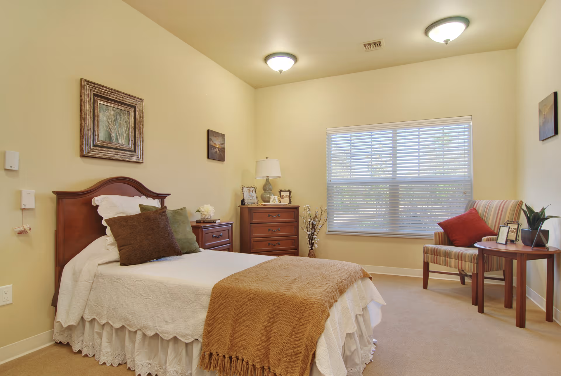 Bright furnished bedroom with a single bed, wooden nightstands, a chair and a large window with blinds.