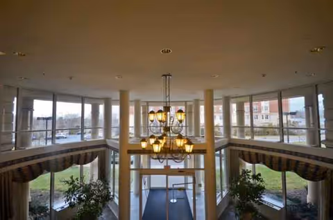 Spacious atrium lobby with large windows, columns, and a central chandelier.