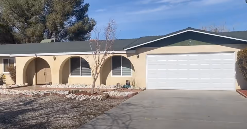 Single-story stucco house with arched front porch, two windows and a two-car garage with a concrete driveway.
