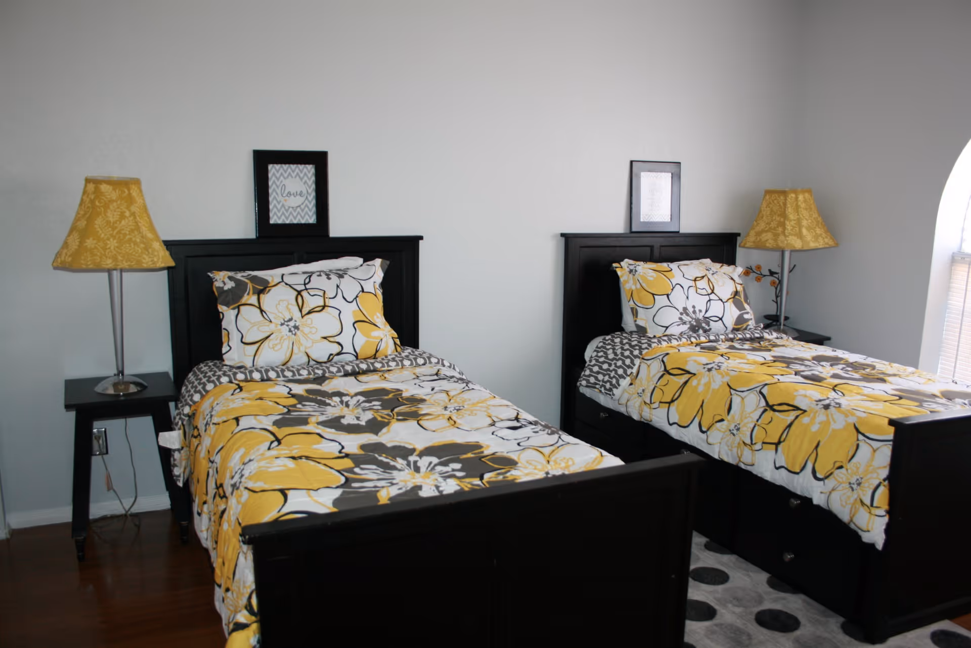 A bedroom with two twin beds featuring matching yellow floral bedding, dark wood headboards, nightstands and lamps.