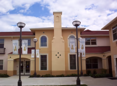 Exterior of a beige senior living building with arched windows, banners, and street lamps.