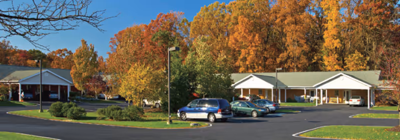 Parking lot in front of single-story buildings surrounded by trees with autumn foliage under a clear sky.