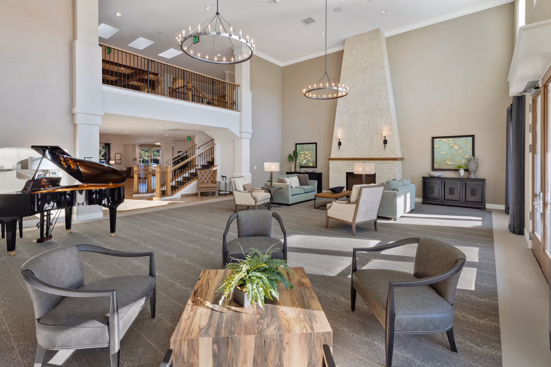 Spacious, well-lit communal lounge with multiple seating areas, a grand piano, high ceilings with chandeliers, and a large fireplace.