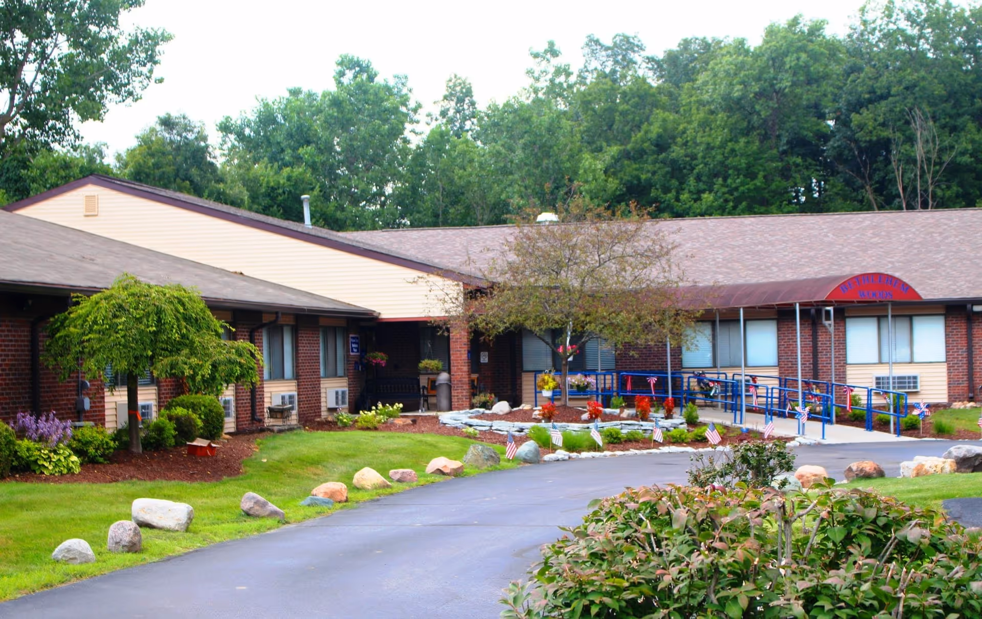 Single-story brick nursing facility with a driveway, landscaped front lawn, wheelchair ramp and trees.