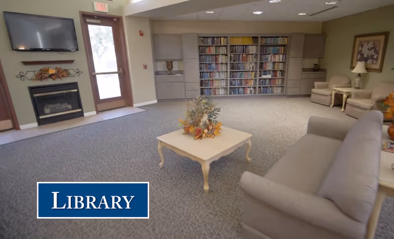 Spacious interior library/common room with sofas, a coffee table, bookshelves, fireplace, and seating.