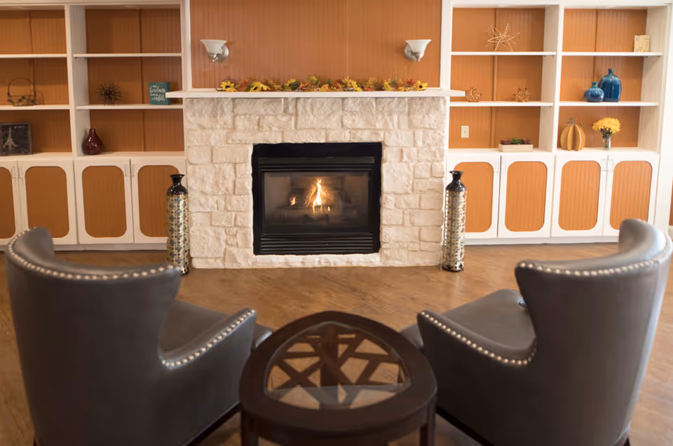 Two armchairs facing a lit stone fireplace with built-in shelving and decorative accents.