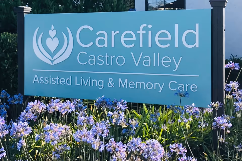 Outdoor sign for Carefield Castro Valley Assisted Living & Memory Care surrounded by purple flowers and green plants.