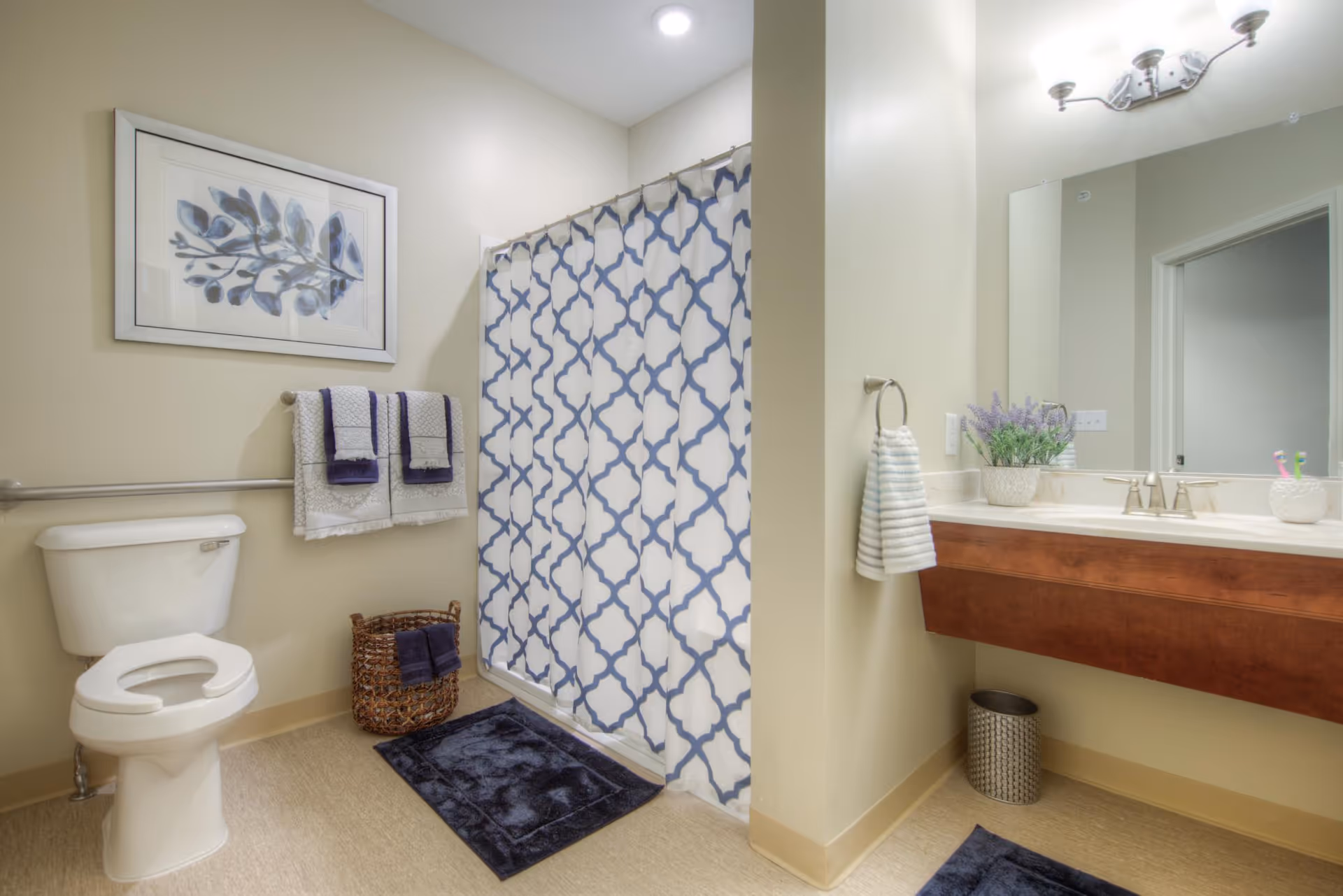 A clean, well-lit bathroom with a toilet, patterned shower curtain, sink vanity, towels, and decorative accents.