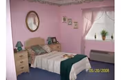 Pink-walled bedroom with a bed, dressers, and a window with sheer curtains.