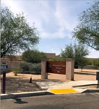 Outdoor view of the entrance sign for Mountain Trace Terrace, surrounded by trees and landscaping under a partly cloudy sky.