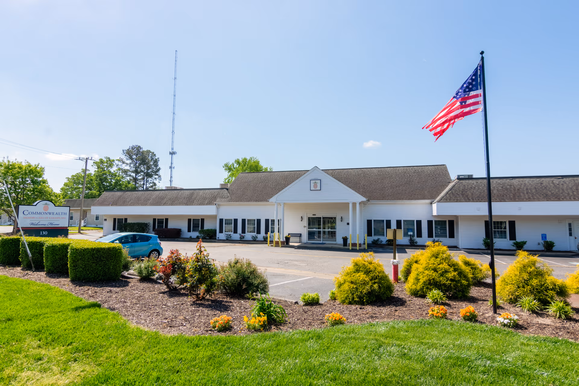 White single-story memory care building with front entrance, American flag, and well-kept landscaping.