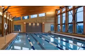 Indoor lap swimming pool with marked lanes, large windows and a wood-beamed ceiling in a well-lit recreation area.