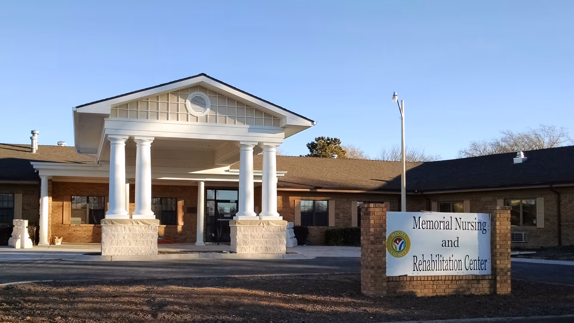 Exterior front view of Memorial Nursing and Rehabilitation Center building with a covered entrance supported by white columns and a sign displaying the facility's name in front.