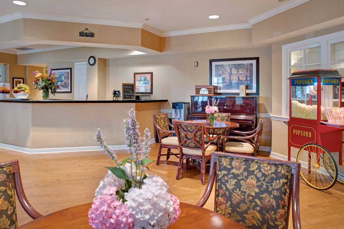 Communal lounge with round tables and floral centerpieces, a piano, popcorn cart, and a reception desk.