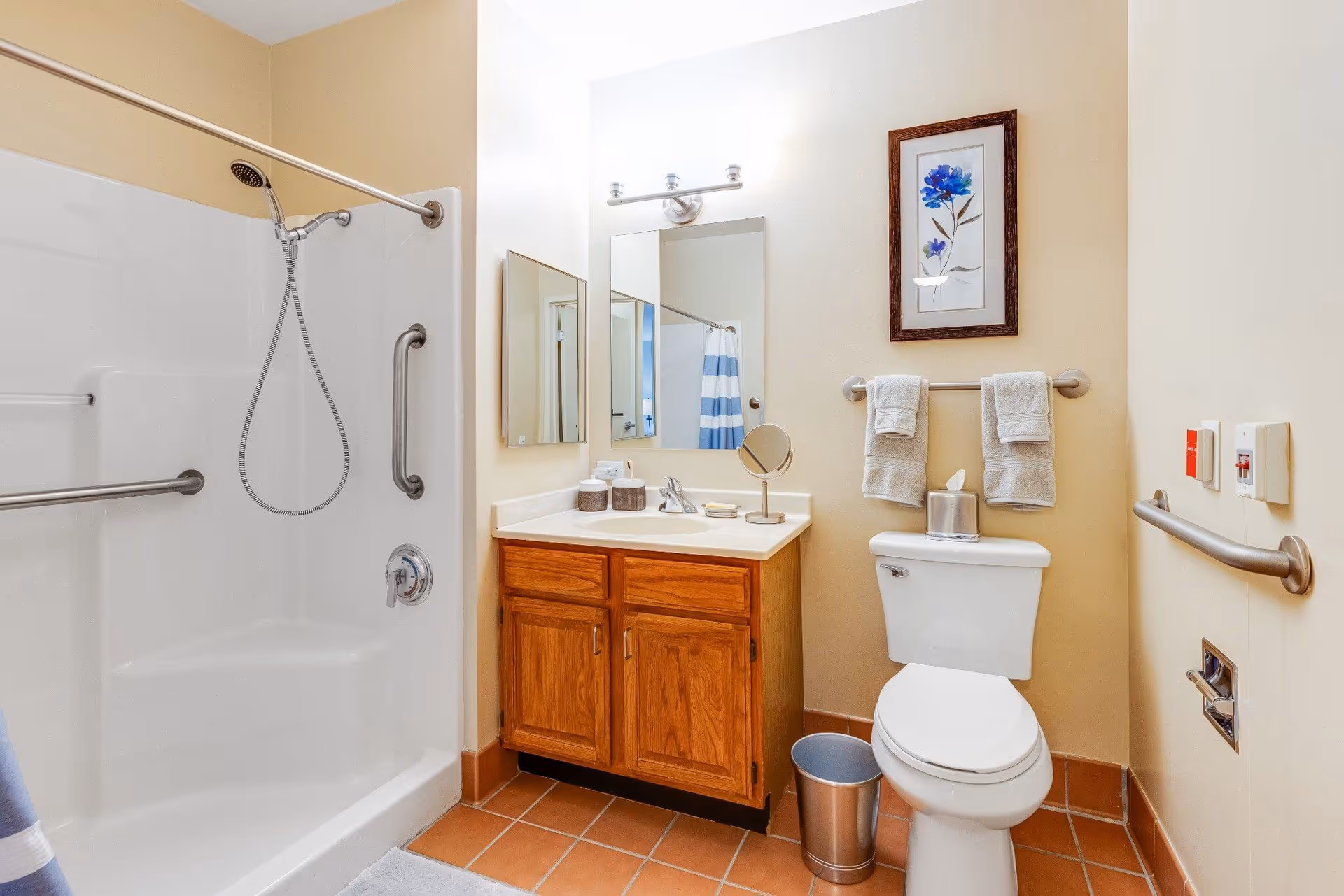 Bathroom with a shower/tub and grab bars, wooden vanity with mirror, and a toilet with towel rack and linens.