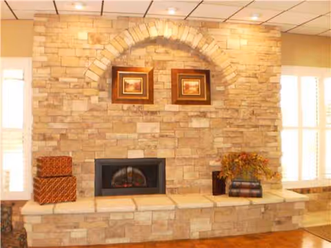 Stone fireplace with arched brick surround and framed artwork in a bright living room.