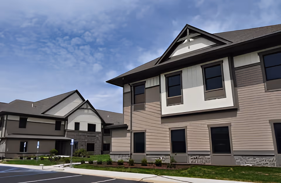 Exterior view of a two-story beige and gray retirement community building under a partly cloudy sky.