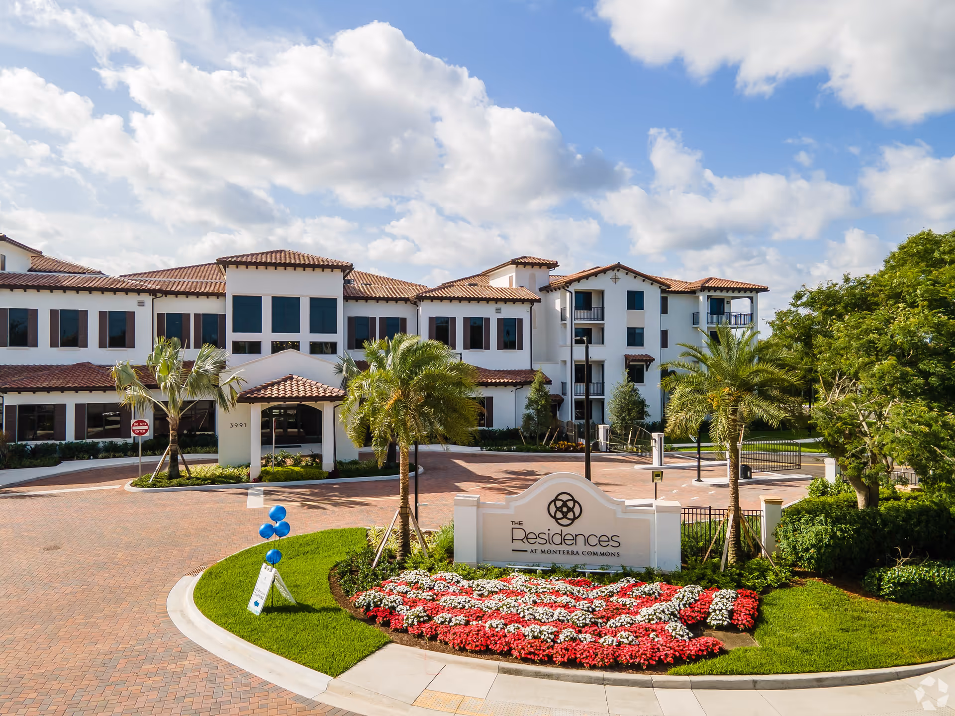 Mediterranean-style senior living building front with driveway, palm trees and a sign reading "The Residences at Monterra Commons".
