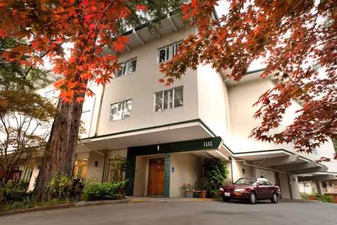 Exterior view of WindChime of Marin Memory Care building with entrance, trees, and a parked car.