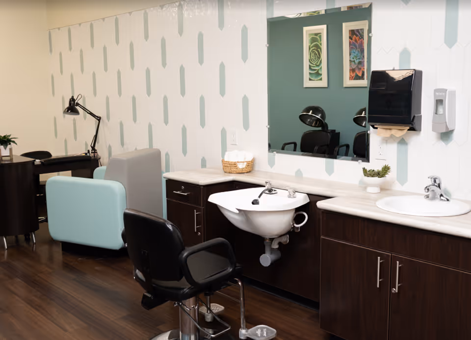 Hair salon station with styling chairs, wash sinks, mirrors, and cabinetry in a senior living facility.