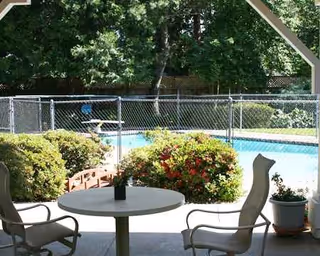 Outdoor patio seating with a round table and chairs overlooking a fenced pool.